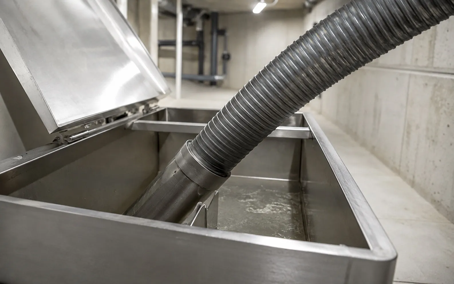 Bac à graisse en inox ouvert dans un local technique, tuyau d'aspiration engagé pour la vidange